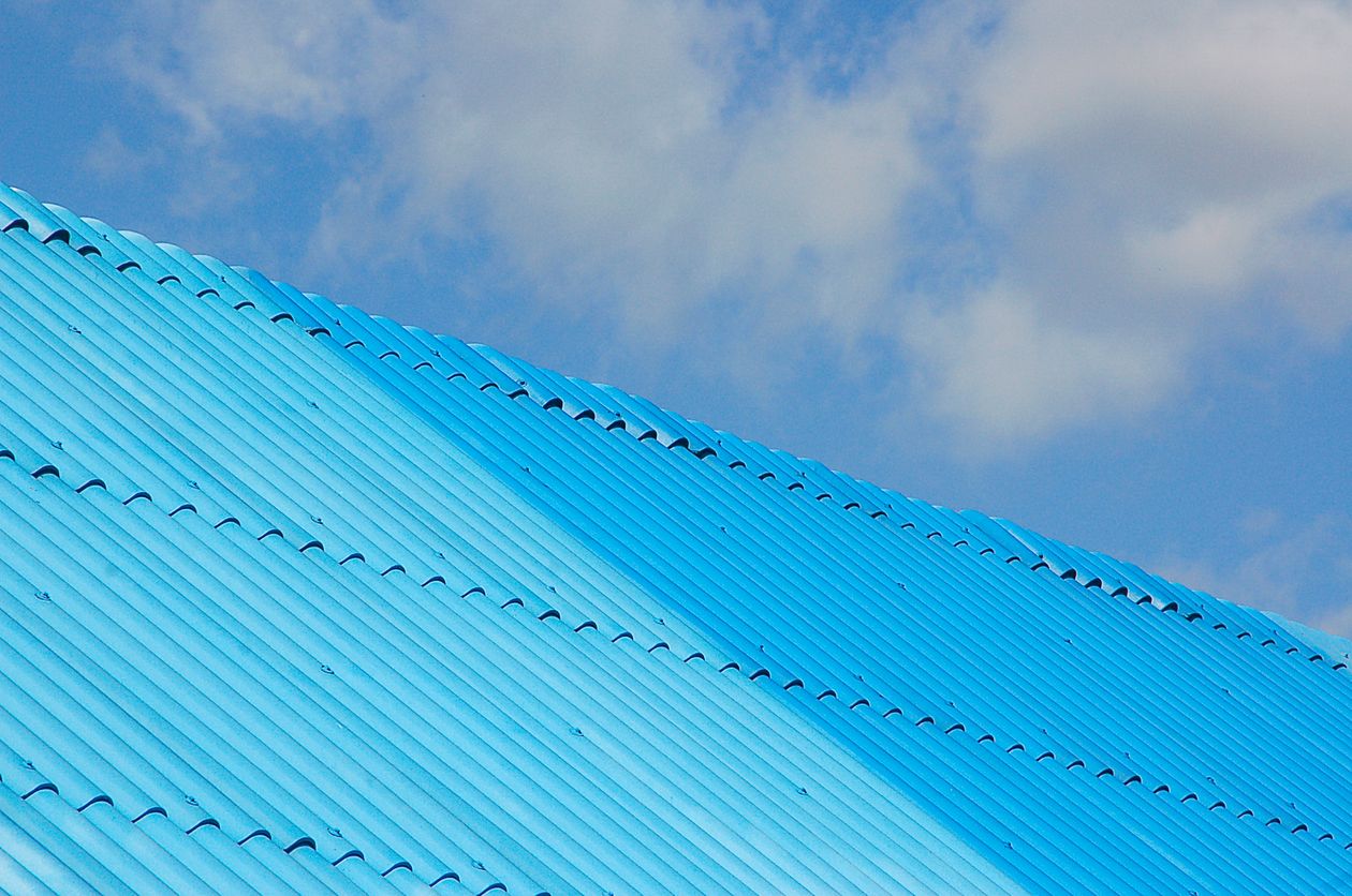 Blue corrugated metal roof under a partly cloudy sky